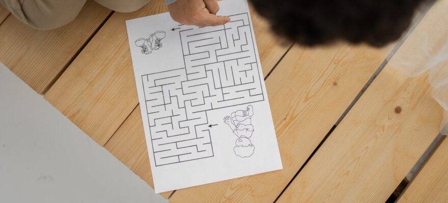 unrecognizable child solving labyrinth test printed on paper at home