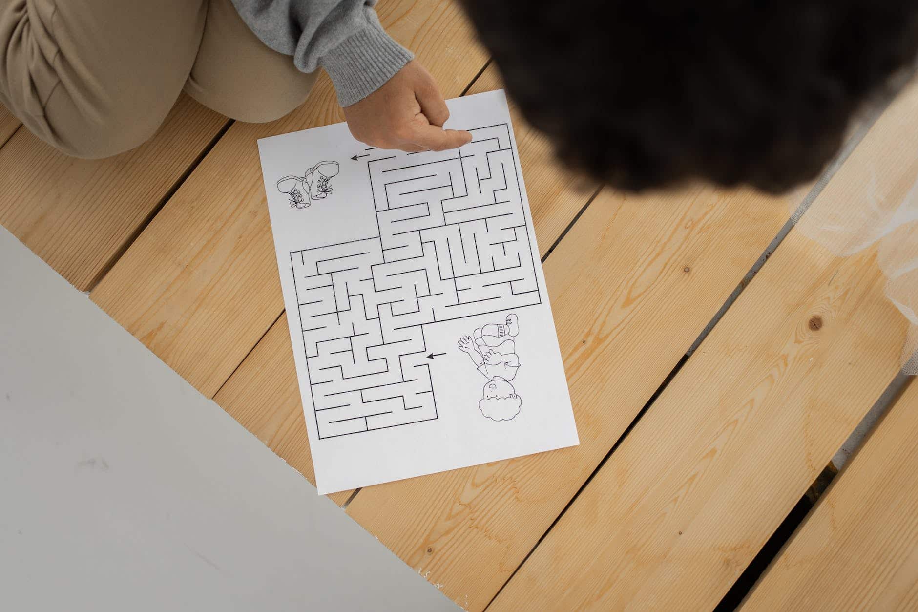 unrecognizable child solving labyrinth test printed on paper at home