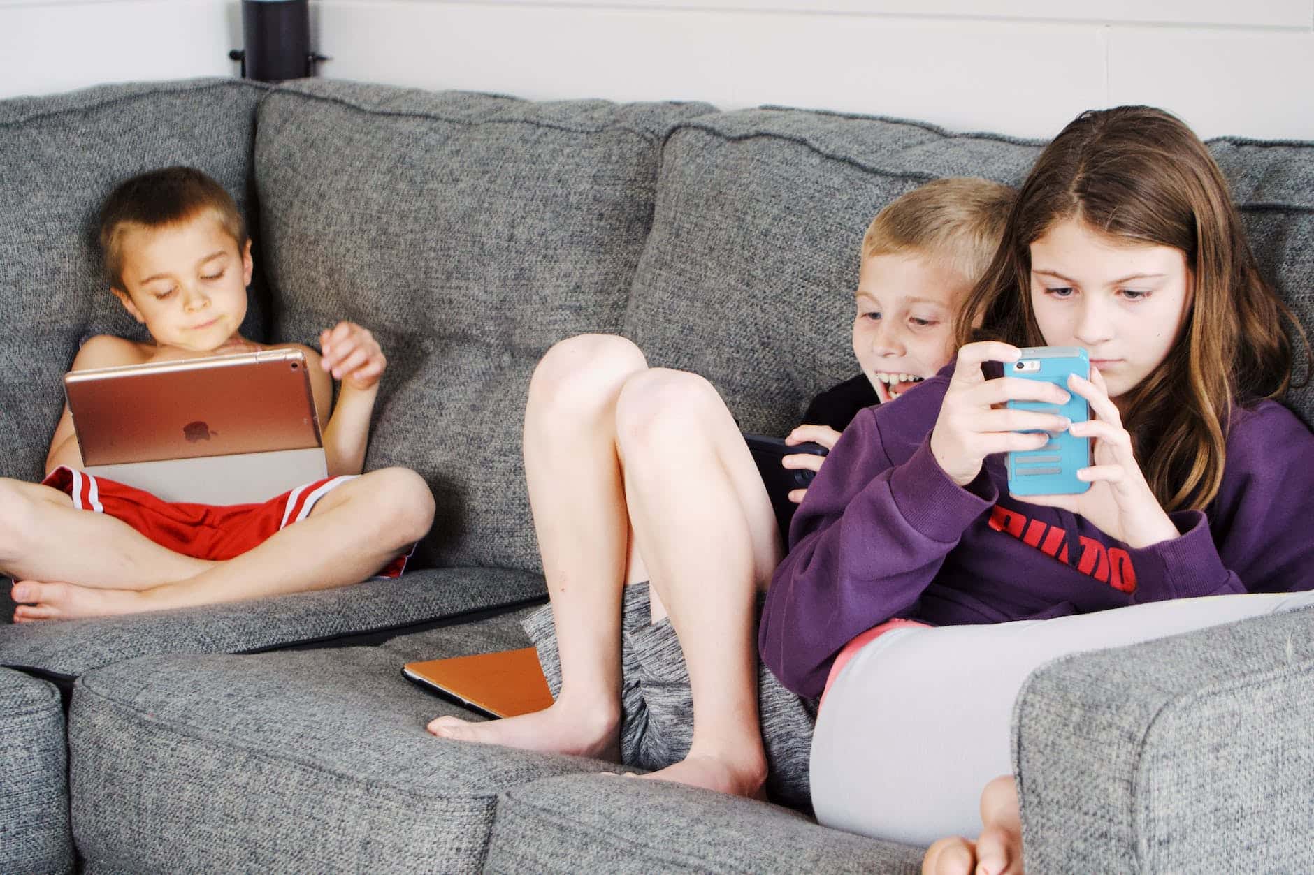 children lying on sofa and using gadgets